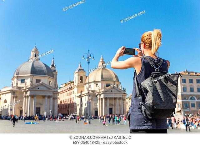 Female tourist with a fashinable vintage hipster backpack taking photo of Piazza del Popolo, People's Square, in Rome, Italy by her mobile phone