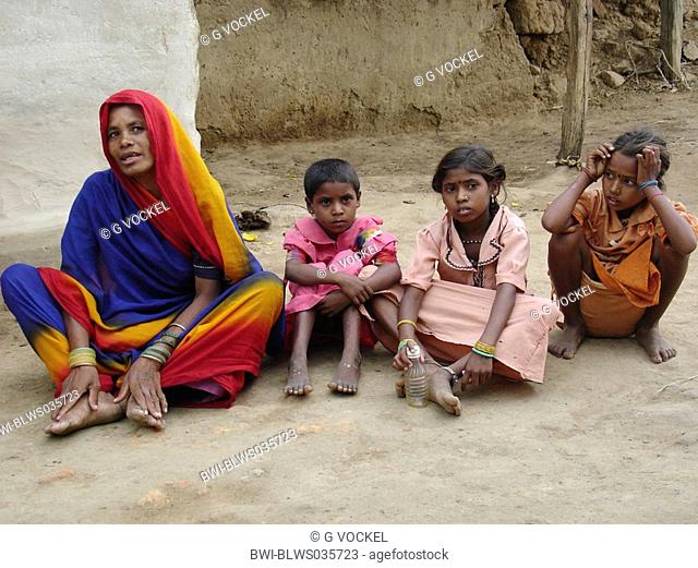 Mother and children in front of a mud hut in a very remote and poor village in central India, India