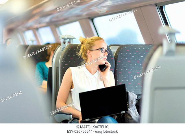 Businesswoman talking on cellphone and working on laptop while traveling by train. Business travel concept