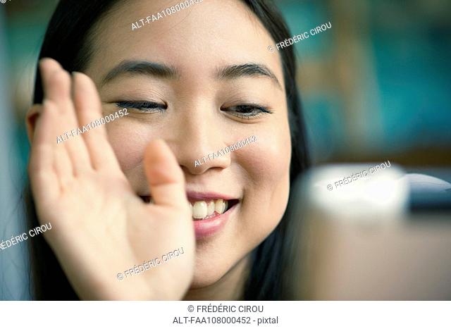 Young woman waving at camera while video conferencing on digital tablet