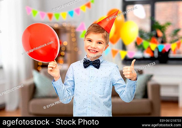 boy in birthday cap with balloon showing thumbs up