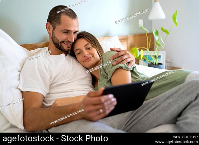 Smiling young couple using digital tablet while lying on bed at home