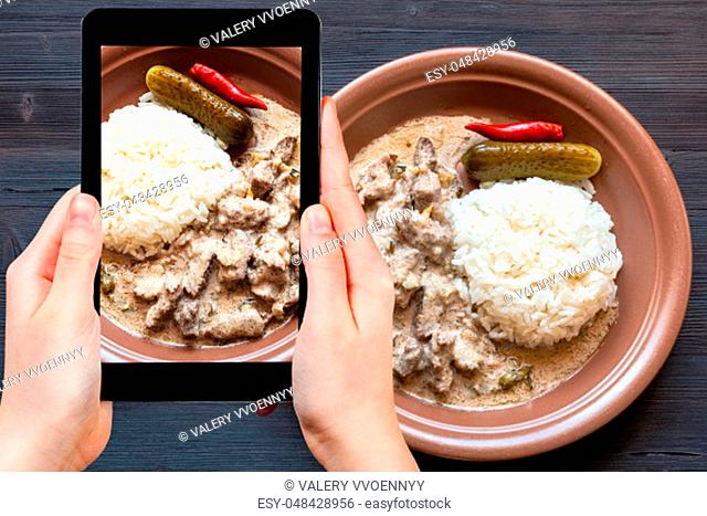 travel concept - visitor photographs of Russian cuisine dish of Beef Stroganoff (Beef Stroganov, Befstroganov) pieces of stewed meat in sour cream with boiled...