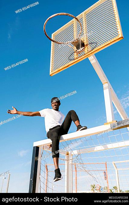 Carefree young man sitting on net against clear sky in court during sunny day