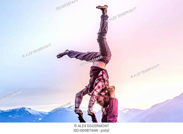 Two young women practicing acroyoga in front of mountain range at sunset, Squamish, British Columbia, Canada
