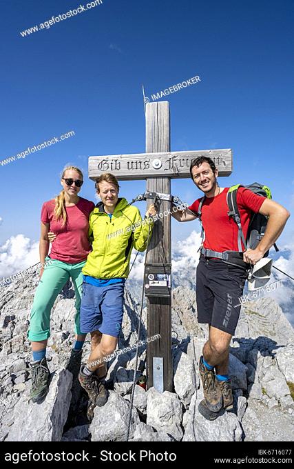 Three hikers at the summit cross of the Hochkalter, Berchtesgaden Alps, Berchtesgadener Land, Upper Bavaria, Bavaria, Germany, Europe