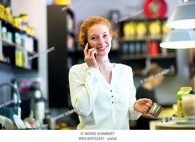 Young woman working in coffee shop, using phone