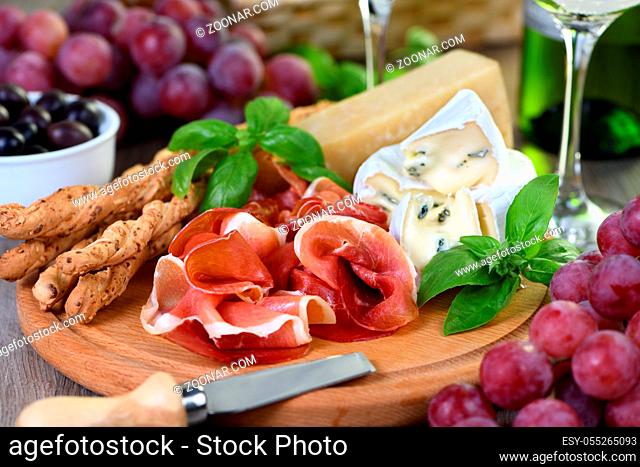 Antipasto. Wine set snacks of dried ham, camembert cheese with mold, parmesan with grissini, olives and pink grapes