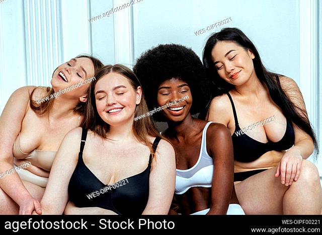Happy multi-ethnic group of models in lingerie with eyes closed sitting against white wall