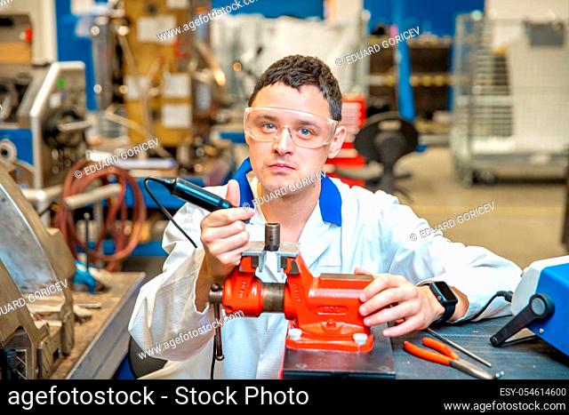 worker in metal processing plant grinds metal component on vise