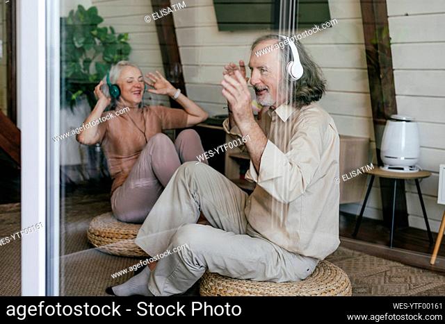 Couple sitting on hassock enjoying music through headphones at home