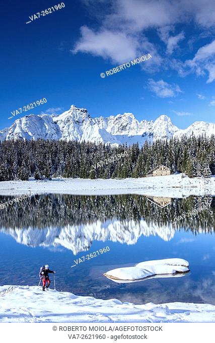 Hiker proceeds on the shore of Lake Palù surrounded by snowy peaks and woods Malenco Valley Valtellina Lombardy Italy Europe
