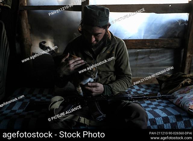 10 December 2021, Syria, Latakia: A Fighter from the armed Syrian opposition (the National Liberation Front) carries a cat as he sits inside a breakroom on the...