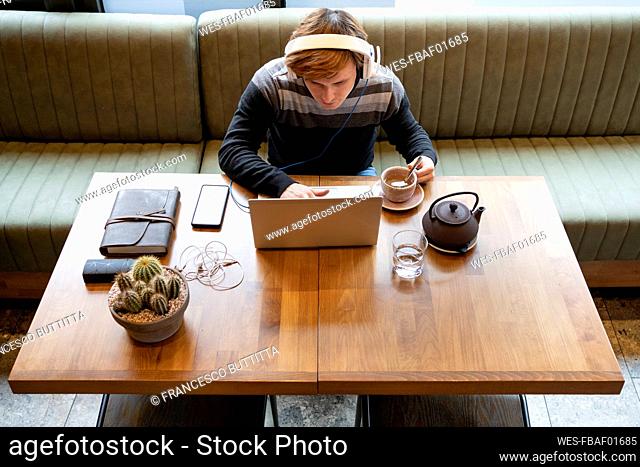 Businessman using laptop by teacup while sitting at desk in office