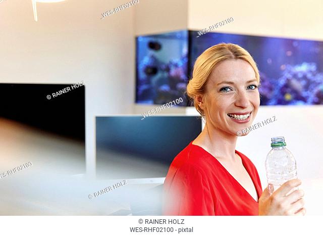 Portrait of smiling young woman drinking water from bottle in office