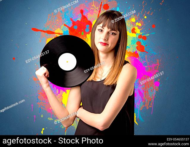 Young lady holding vinyl record on a grey background with colorful splashes behind her