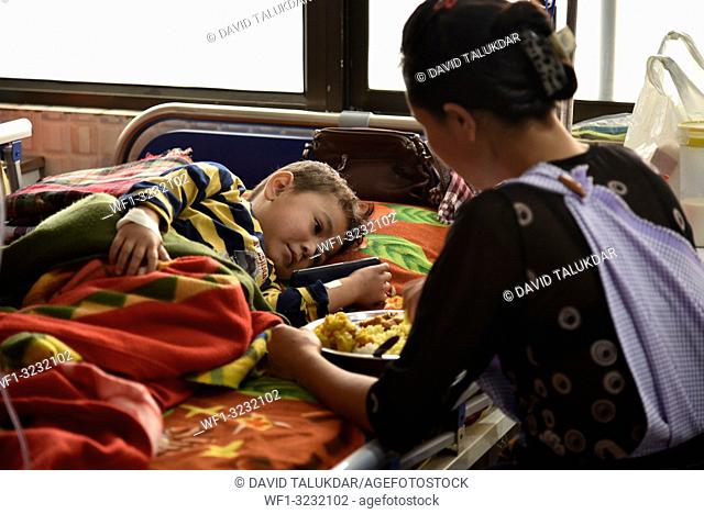 World Cancer Day. Guwahati, Assam, India. 4 February 2019. A Child Cancer patient Waching cartoon in mobile phone and mother feeding on his bed at Dr