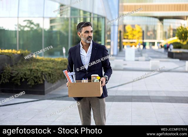 Businessman with office supply in box standing on footpath