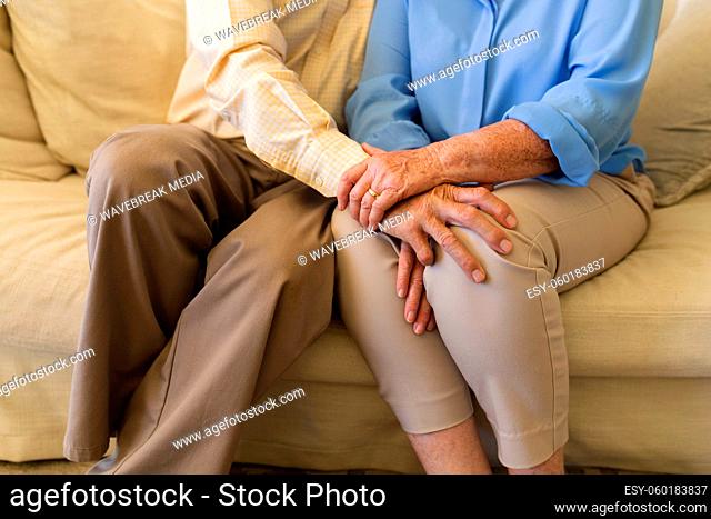 Mid section of senior caucasian couple sitting on sofa holding hands