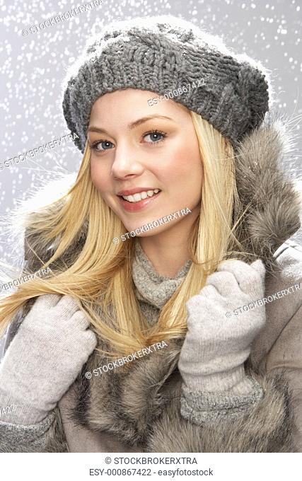 Fashionable Teenage Girl Wearing Cap And Fur Coat In Studio With Snow
