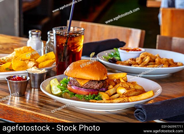 Home made hamburger with beef, onion, tomato, lettuce and cheese. Fresh burger closeup on wooden rustic table with potato fries, beer and chips