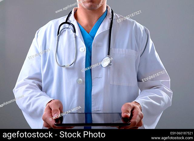 Midsection of caucasian male doctor using tablet, isolated on grey background