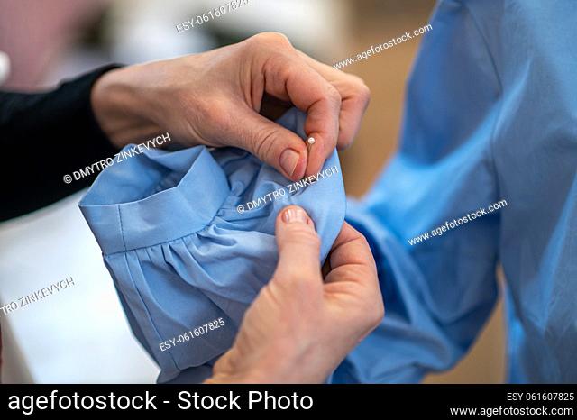Handmade. Close-up of experienced tailors hands with pin piercing sleeve of blouse indoors, no face