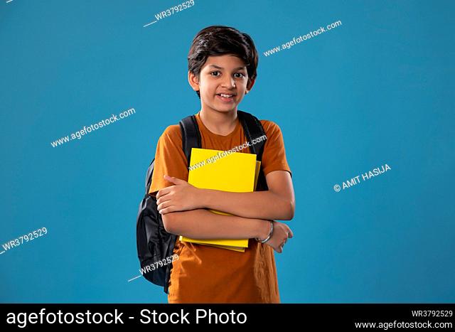 Portrait of smiling boy holding books while standing against blue background