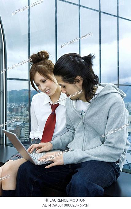Young couple sitting on windowsill, using laptop computer