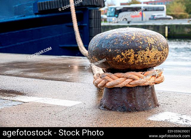 a ship is attached with a thick rope to a bollard in the harbour