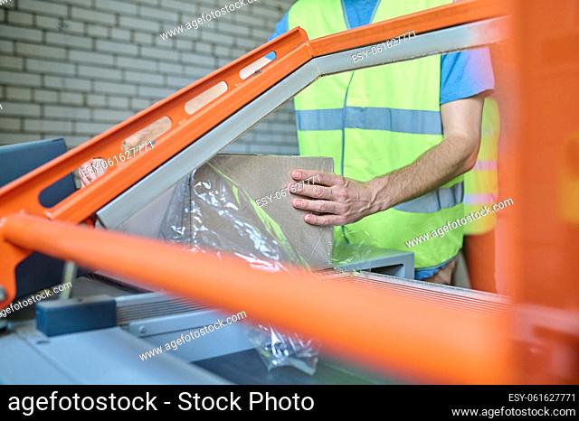Cropped photo of a warehouse operator putting the cardboard box into the film wrapping machine