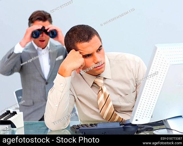 Ethnic businessman looking his colleague's computer through binoculars