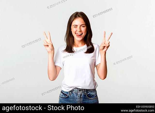 Cheerful cute brunette girl showing peace gestures and winking happy