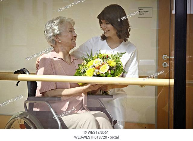 Germany, Cologne, Caretaker giving bouquet to senior women on wheelchair in nursing home