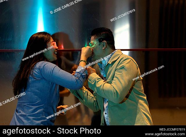 Happy mature couple wearing smart glasses punching each other by metal wall