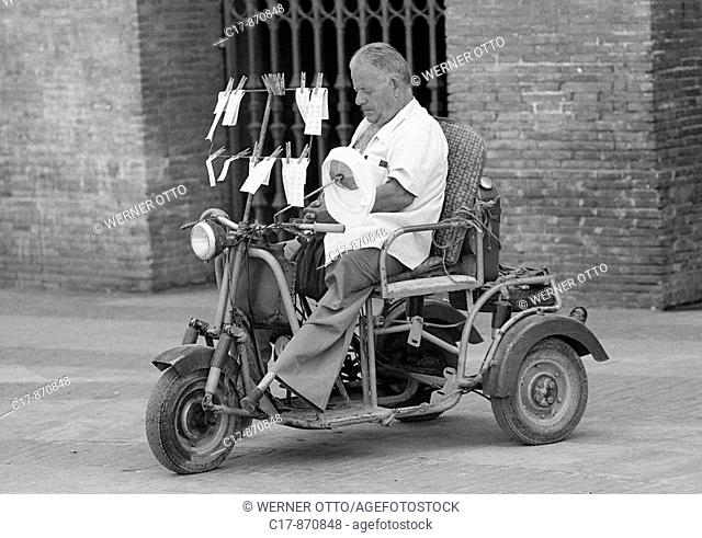 Seventies, black and white photo, people, poorness, gambling, ticket seller on a motorbike, physically handicapped, artificial leg, aged 50 to 70 years, Spain