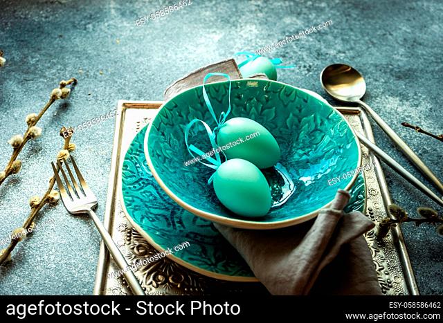 Festive holiday table setting for Easter dinner decorated with colored eggs on stone background with copy space