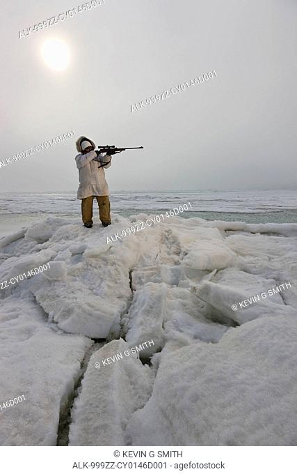 Female Inupiaq Eskimo hunter wearing a Eskimo parkaAtigi aims a rifle towards the open water of the Chukchi Sea, Barrow, Arctic Alaska, Summer