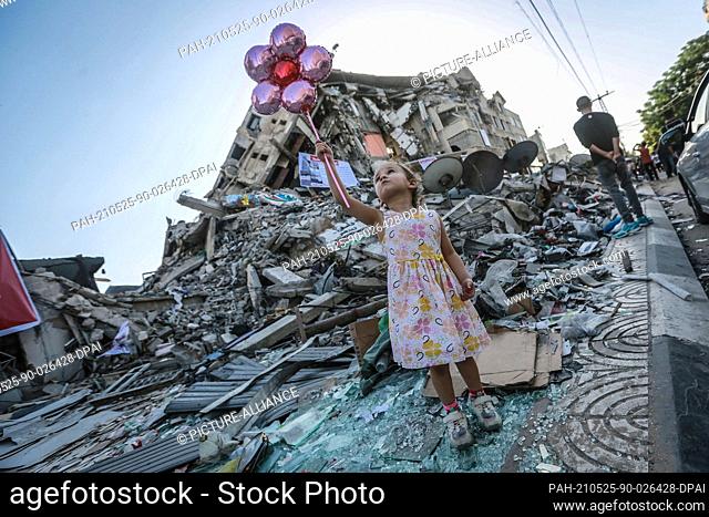 25 May 2021, Palestinian Territories, Gaza City: A girl holds balloons near the Hanadi Tower in the middle of Al-Rimal Market