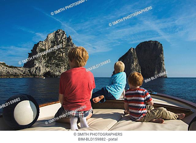 Caucasian brothers on boat admiring rock formations in ocean, Isle of Capri, Naples, Italy