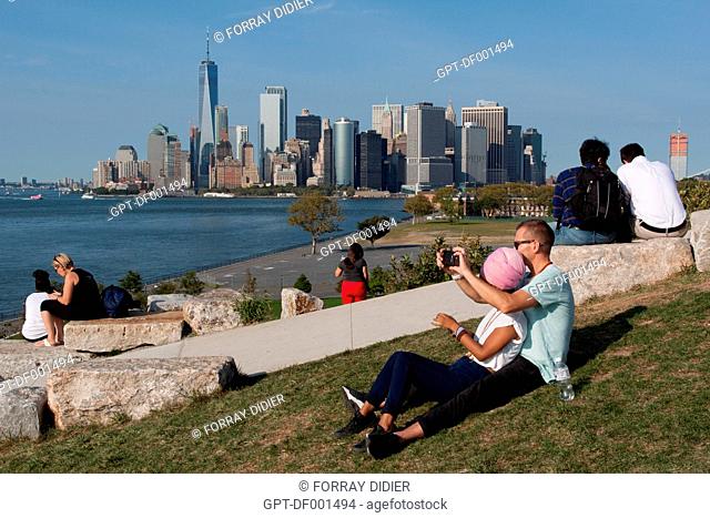TOURISTS AND NEW YORKERS ADMIRING THE VIEW OF THE MANHATTAN SKYLINE AND THE BAY OF NEW YORK FROM THE MAN-MADE HILLS OF GOVERNORS ISLAND, THE HILLS