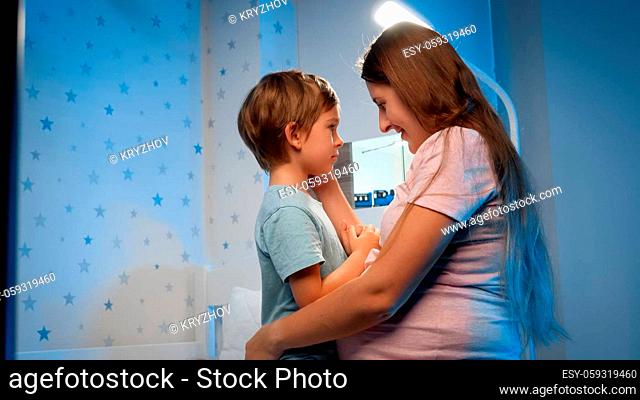 Portrait of young pregnant mother stroking and soothing her scared little son at night