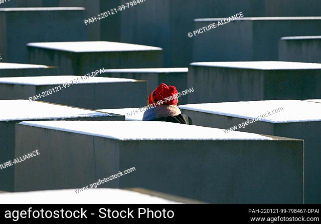 21 January 2022, Berlin: A woman walks past stelae of the Holocaust Memorial covered with fresh snow at temperatures around minus two degrees Celsius