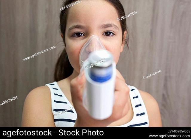 Child girl using medical spray for breath. Inhaler, spacer and mask. Front view