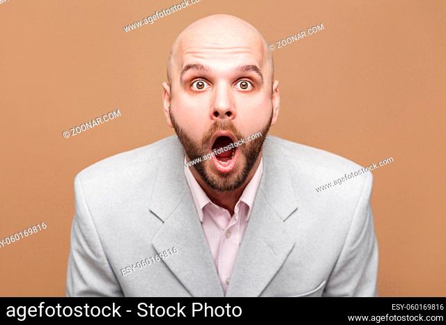 are you serious? Portrait of handsome middle aged bald bearded businessman in classic light gray suit standing looking at camera with amazed face
