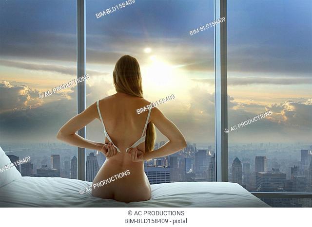 Caucasian woman undressing and admiring cityscape in window