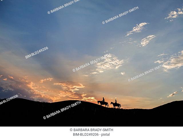Silhouette of Caucasian couple riding horses at sunset