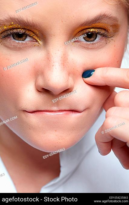 Closeup shot of human female face. Woman with unusual glitter glitzy vogue face beauty makeup. Girl with yellow smoky eyes eye shadows and hand near face