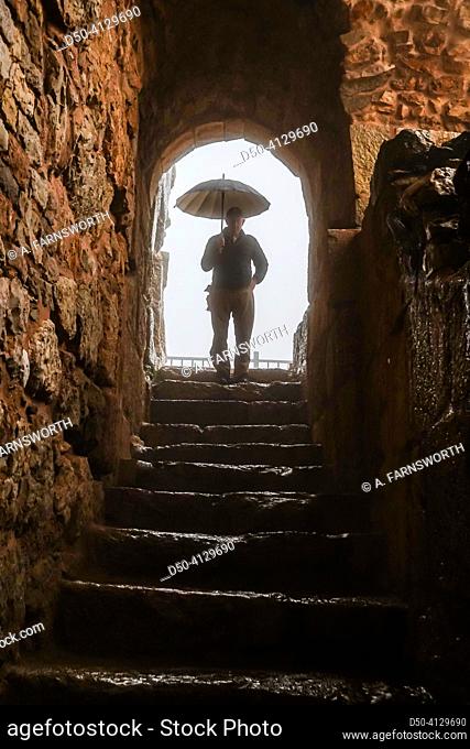 Ajlun, Castle, Jordan A tourist with umbrella visits the castle under an arch in the rain