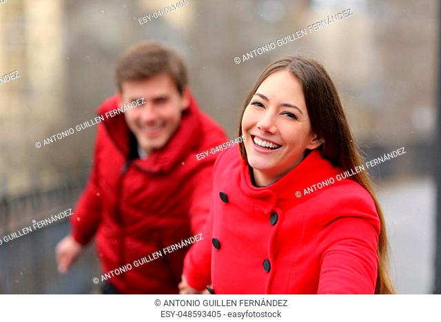 Happy couple in red running outdoors towards camera in the street in winter